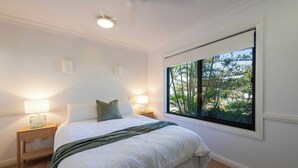 A bedroom with a large bed, two bedside lamps, a window with a view of greenery, and a ceiling light.