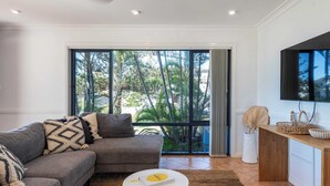 A modern living room with a grey sofa, a round coffee table, and a large window with a view of greenery.