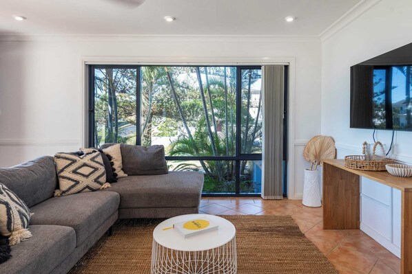 A modern living room with a grey sofa, a round coffee table, and a large window with a view of greenery.