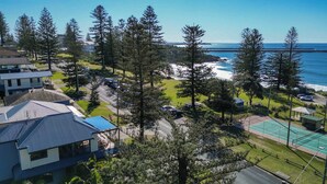 A coastal property with a view of the ocean, a tennis court, and several buildings.