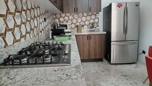 Una cocina con estufa a gas, horno empotrado, refrigerador de acero inoxidable, armarios de madera y un protector contra salpicaduras estampado.