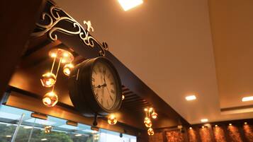 Un reloj con un marco decorativo y luces colgantes, situado en una habitación con vistas al verdor exterior.