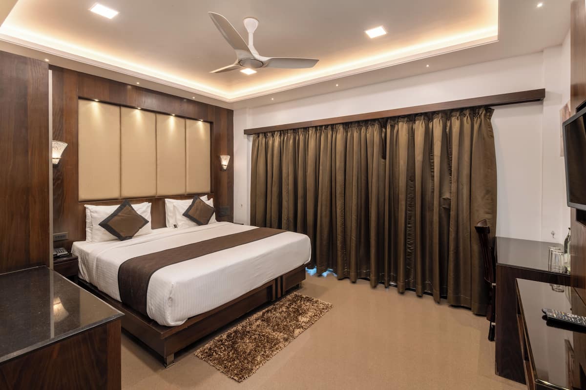 A hotel room with a large bed, a desk, a ceiling fan, and a TV.