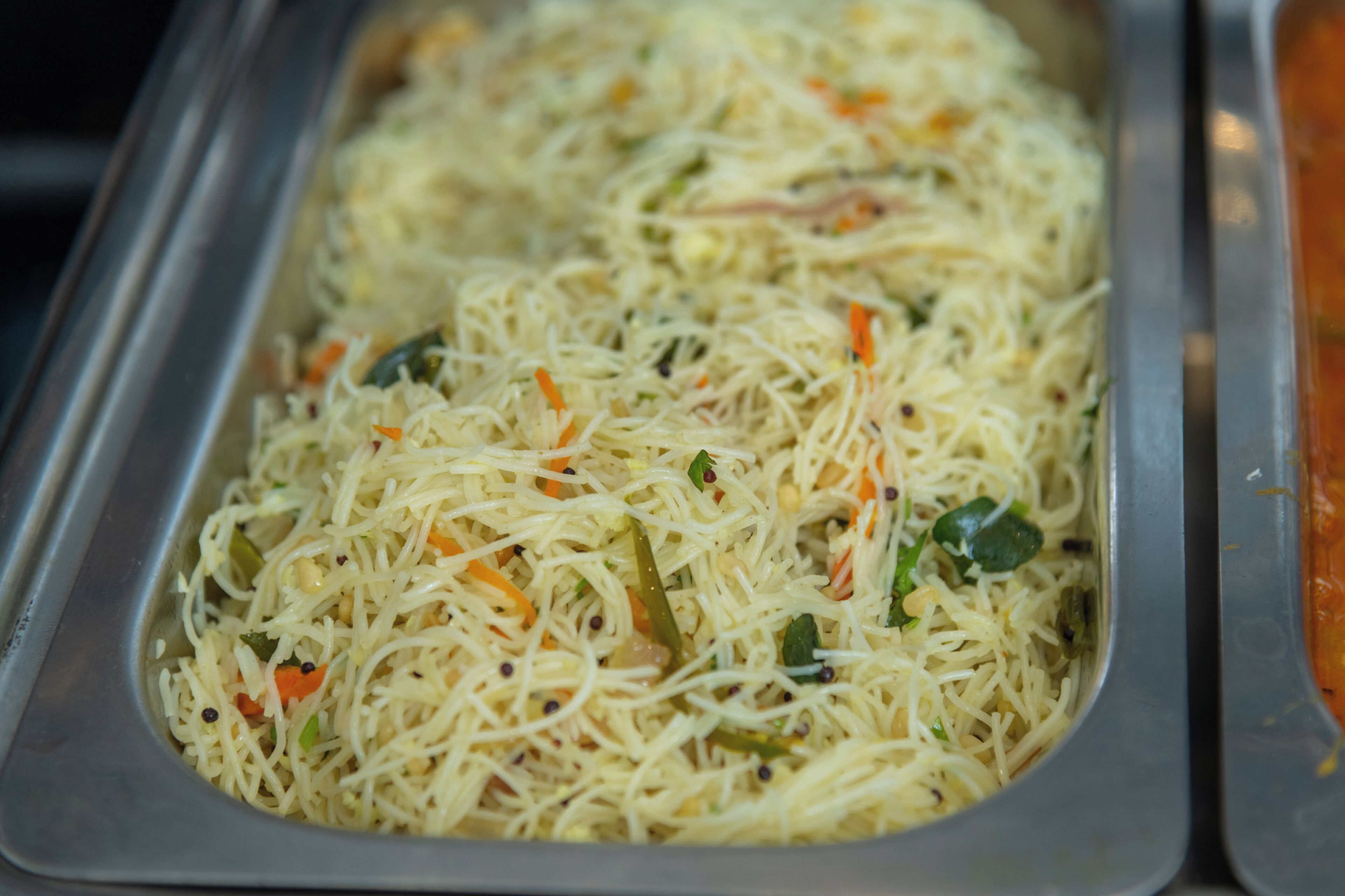 A stainless steel serving dish filled with spaghetti and vegetables.