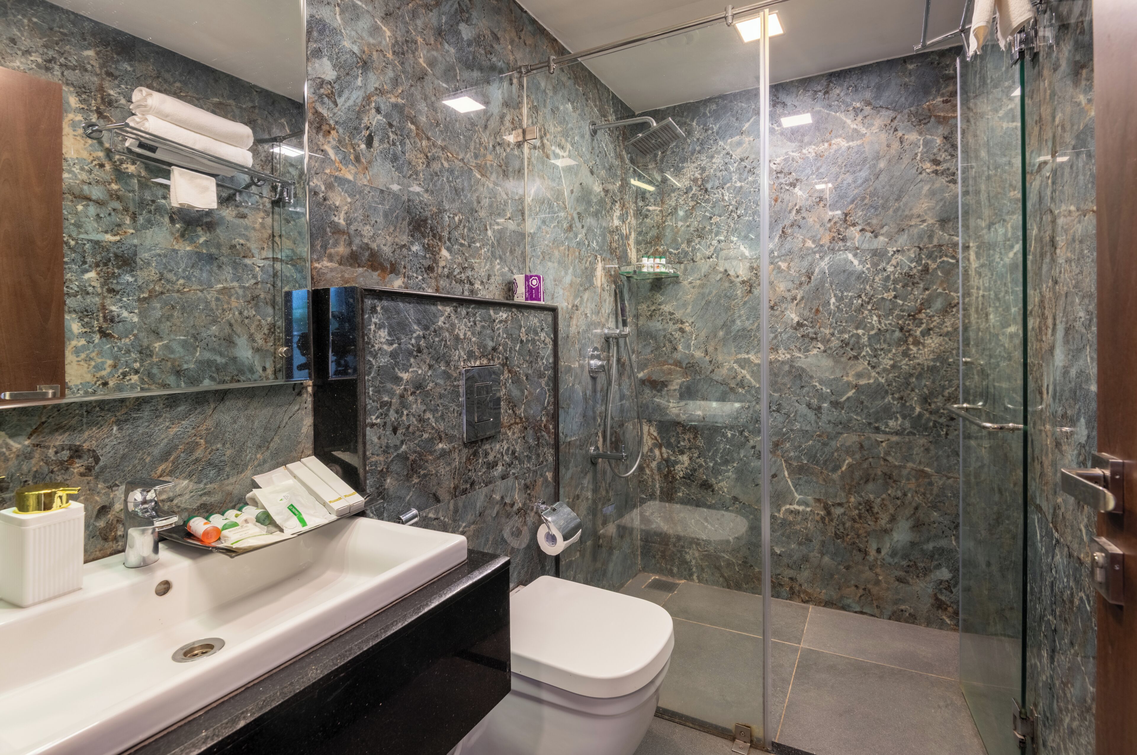 A bathroom with a marble wall, a glass shower enclosure, a white sink, and a toilet.