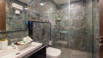 A bathroom with a marble wall, a glass shower enclosure, a white sink, and a toilet.