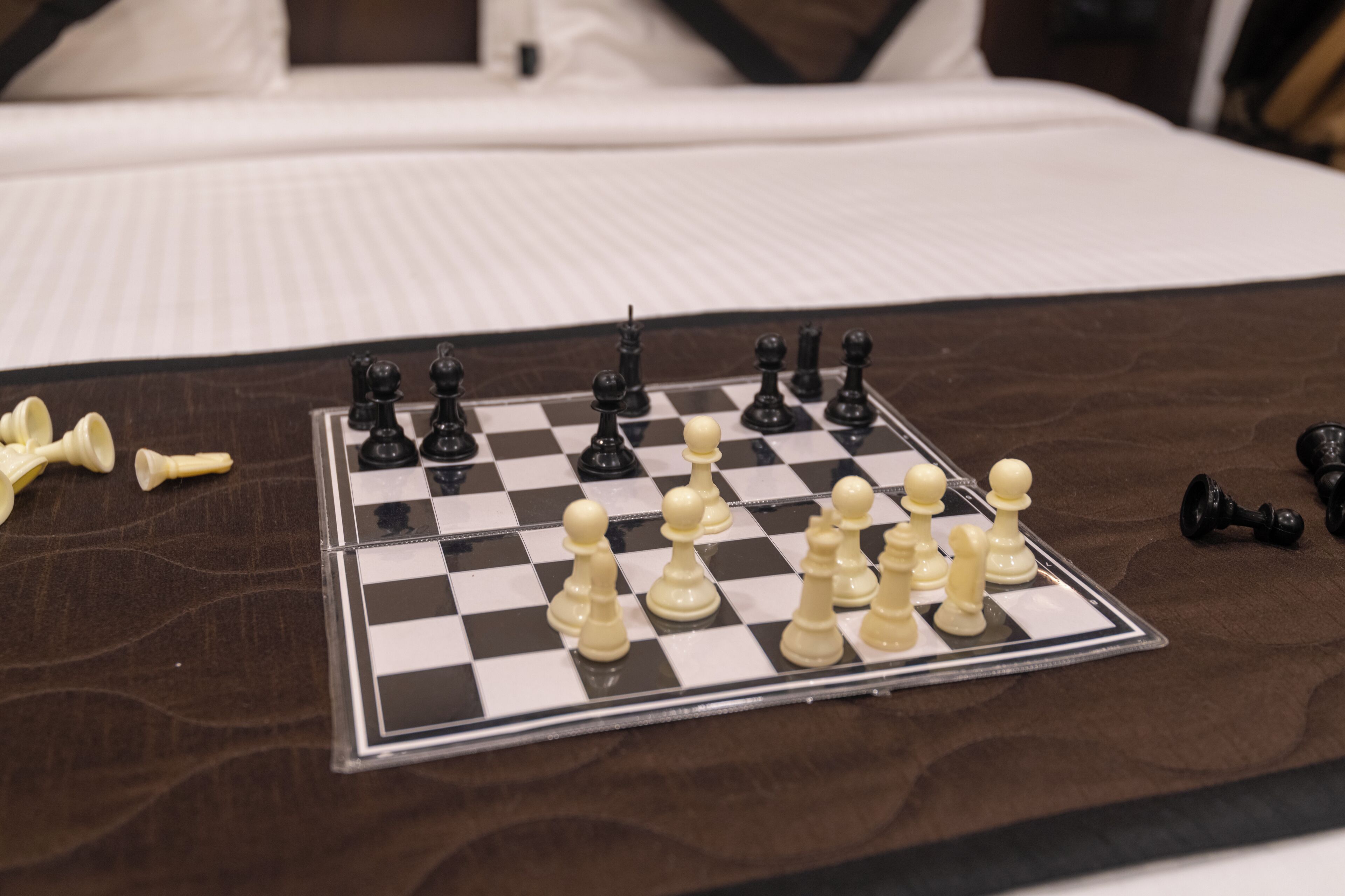 Un tablero de ajedrez sobre una superficie de madera, con una cama al fondo.