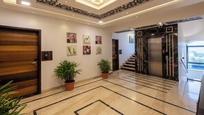 A modern lobby with a wooden door, potted plants, artwork on the walls, a marble floor, and an elevator.