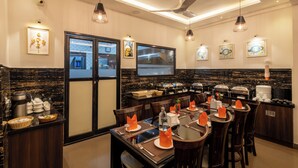 A hotel dining area with a buffet setup, multiple dining tables, and a ceiling fan.