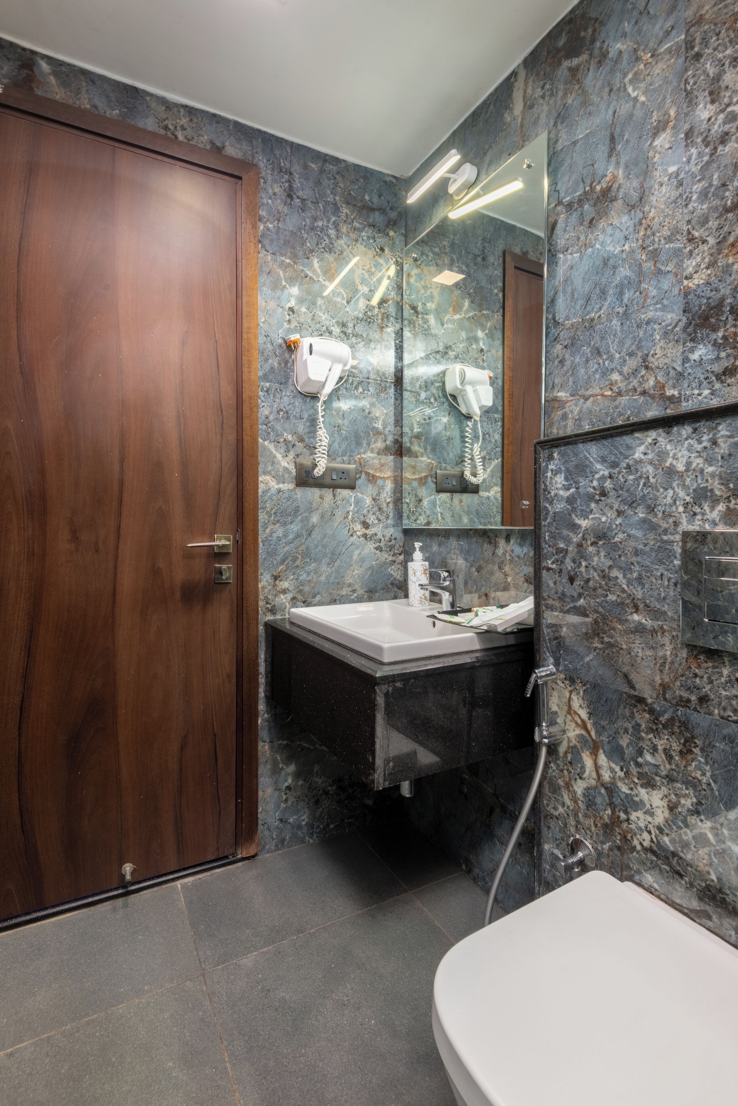 A bathroom with a wooden door, marble walls, a sink, and a mirror.