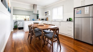 A modern kitchen with white cabinetry, a stainless steel refrigerator, and a wooden dining table with chairs. - Relax and Unwind at Otters Retreat (West Busselton)