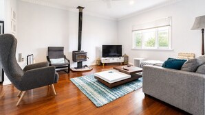 A living room with a fireplace, a sofa, a chair, a TV, and a window. - Relax and Unwind at Otters Retreat (West Busselton)