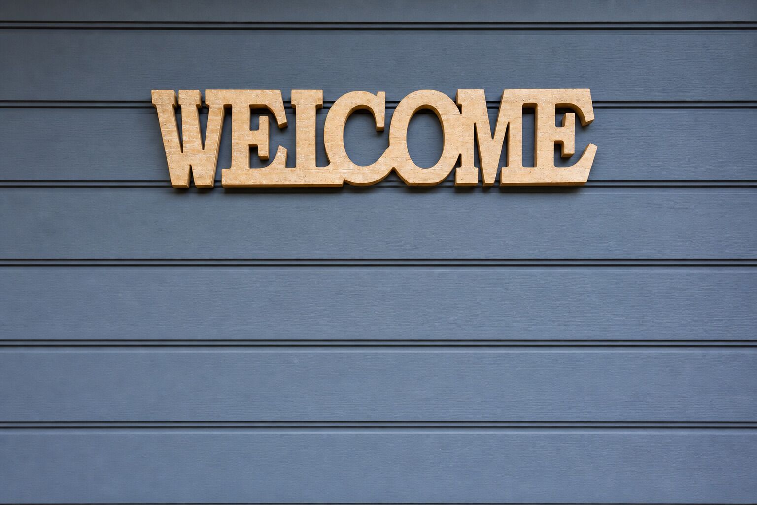 Lettere di legno con la scritta 'WELCOME' su un muro blu.