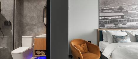 Une salle de bain moderne équipée de toilettes, d’un lavabo et d’une douche. On y trouve un meuble en bois contenant des serviettes, ainsi qu’un tableau encadré accroché au mur.