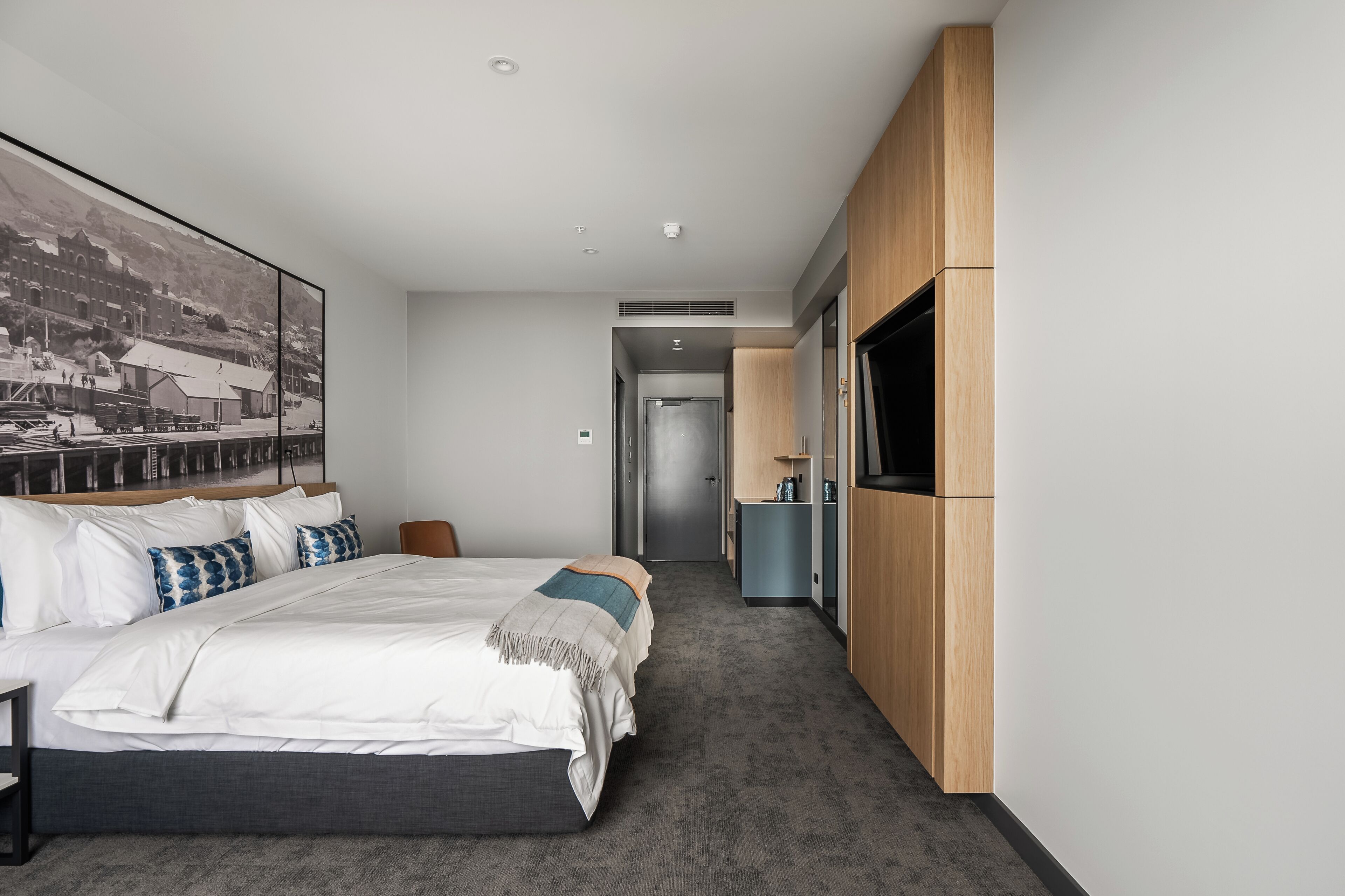 Una habitación de hotel moderna con una cama grande, un televisor montado en la pared y un pasillo que conduce a un baño.