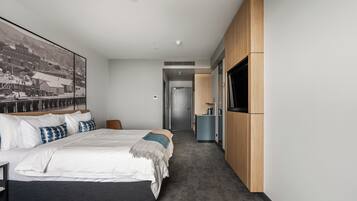 Una habitación de hotel moderna con una cama grande, un televisor montado en la pared y un pasillo que conduce a un baño.