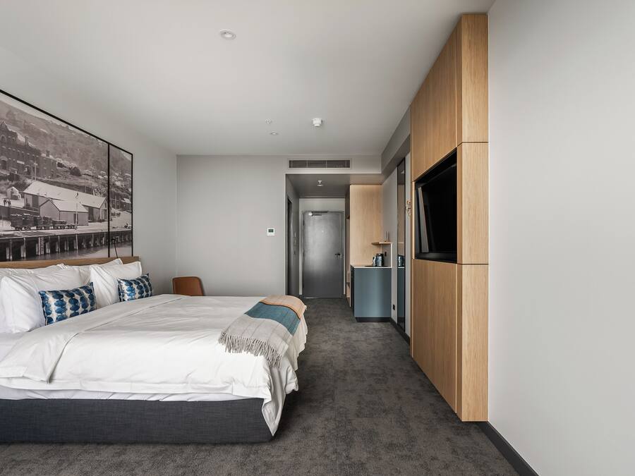 Una habitación de hotel moderna con una cama grande, un televisor montado en la pared y un pasillo que conduce a un baño.