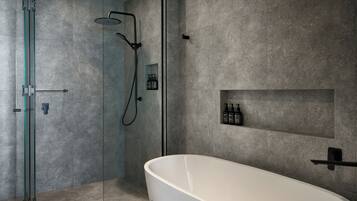 Un bagno moderno con doccia a parete in vetro, una vasca da bagno indipendente e uno scaffale con articoli da toilette.