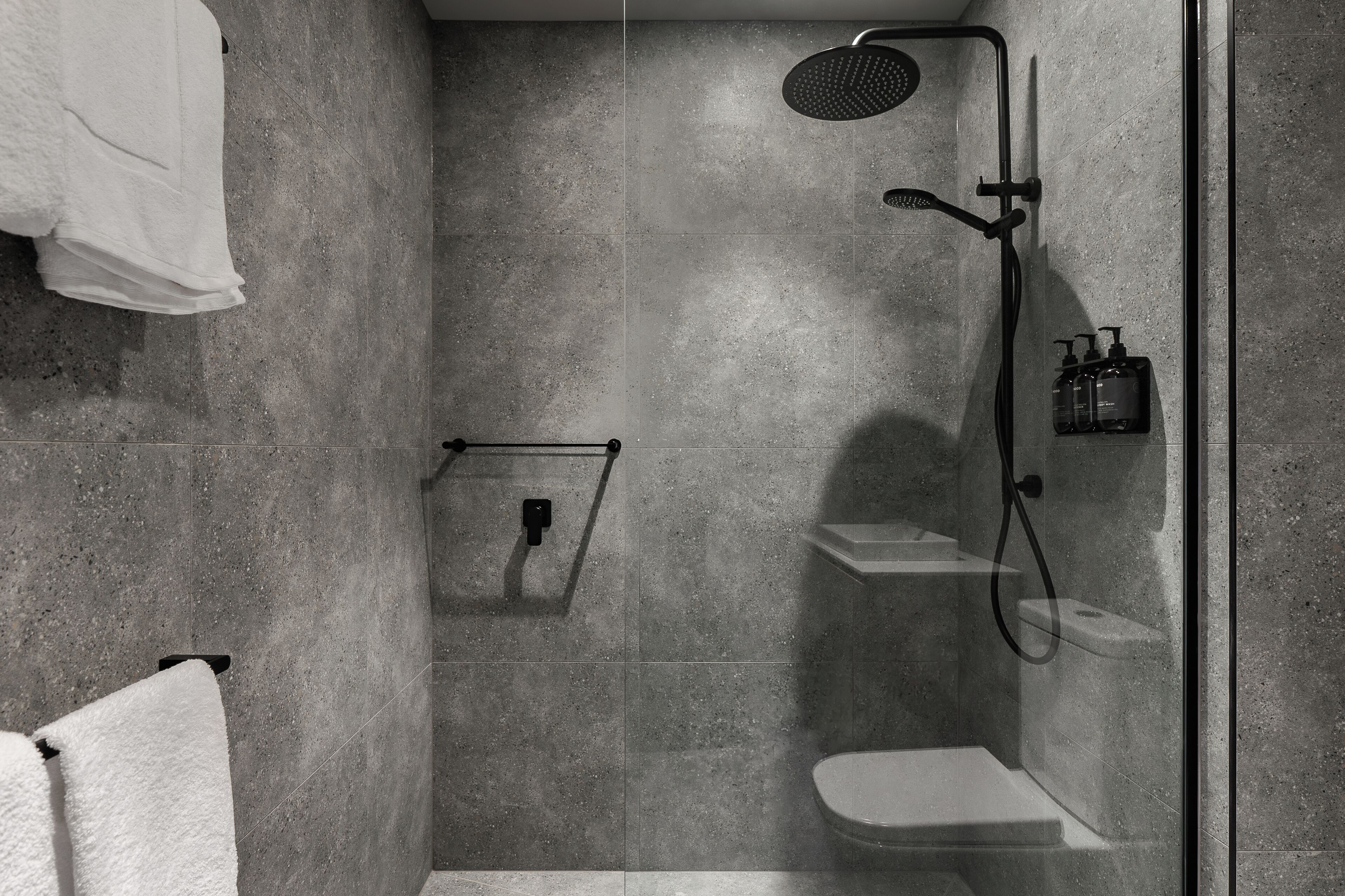 A modern shower area with a glass enclosure, a handheld showerhead, and a built-in seat.