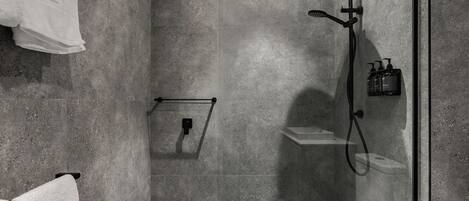 Un área de ducha moderna con cabina de vidrio, ducha de mano y asiento incorporado.