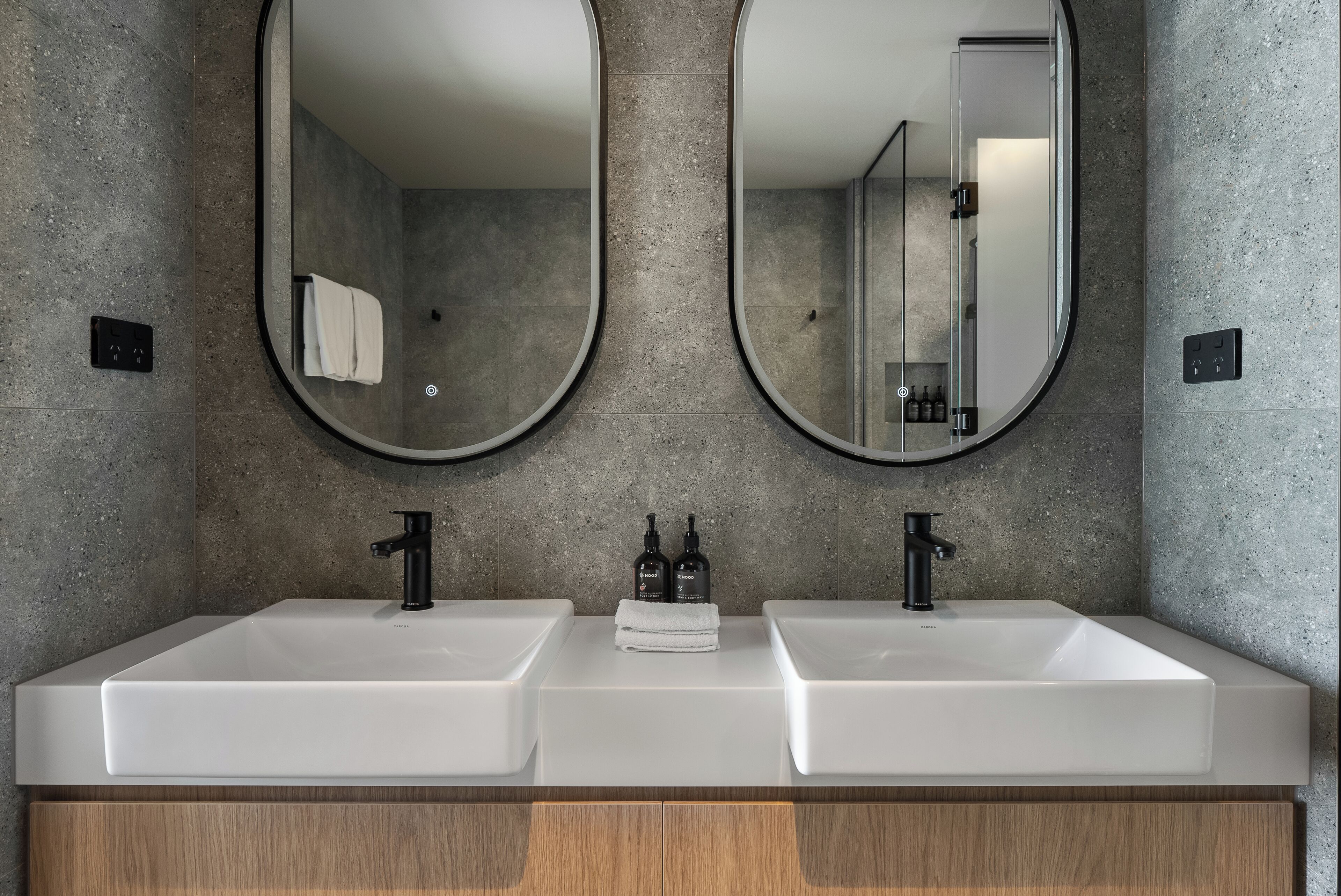 A modern bathroom with two sinks, a mirror, and a towel rack.