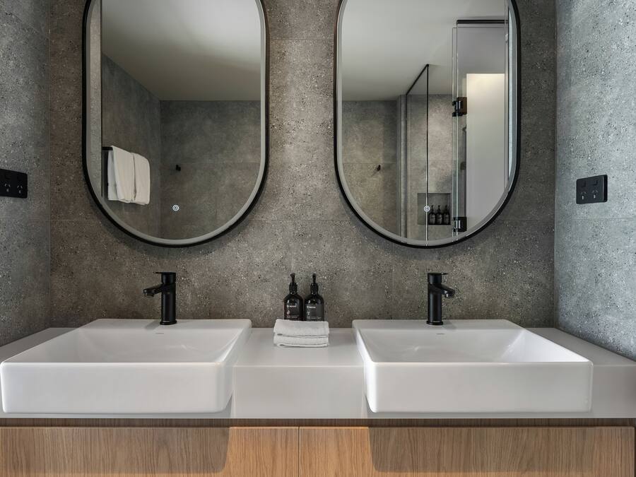 A modern bathroom with two sinks, a mirror, and a towel rack.
