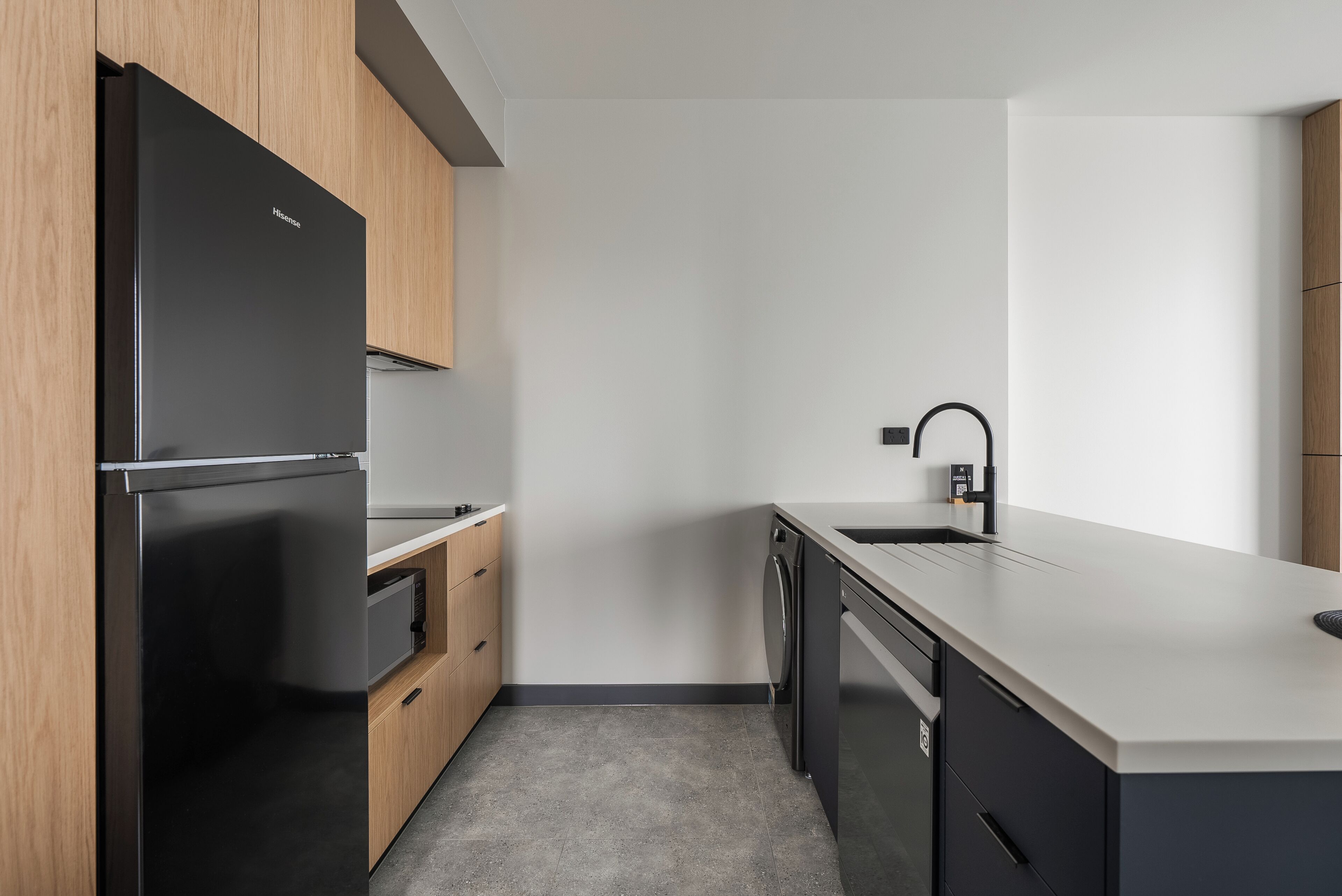 A modern kitchen with a black refrigerator, wooden cabinets, a dishwasher, and a white countertop.