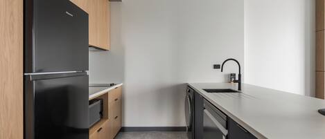 A modern kitchen with a black refrigerator, wooden cabinets, a dishwasher, and a white countertop.