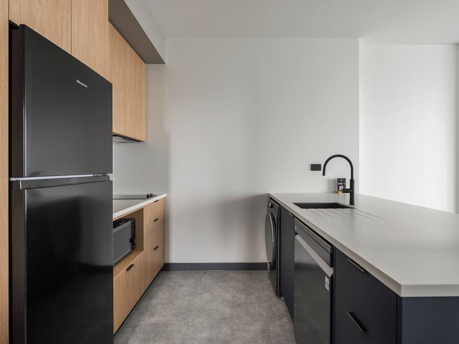 Une cuisine moderne avec un réfrigérateur noir, des armoires en bois, un lave-vaisselle et un plan de travail blanc.