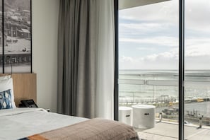 A hotel room with a large bed, a bedside phone, and a view of the ocean through floor-to-ceiling windows. - One North Terrace (Burnie)