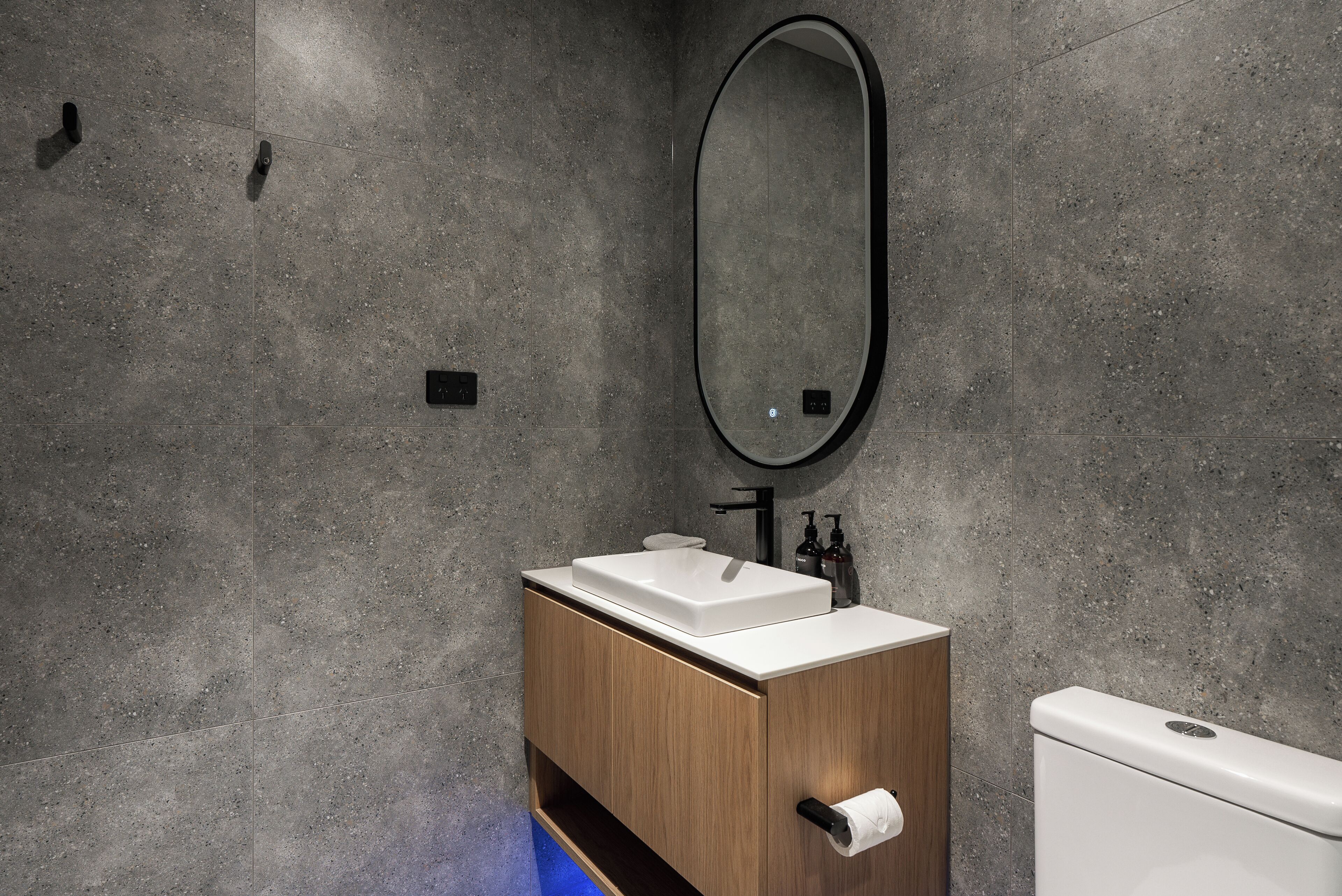 A modern bathroom with a wooden vanity, a white sink, and a large mirror.