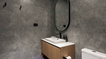 A modern bathroom with a wooden vanity, a white sink, and a large mirror.