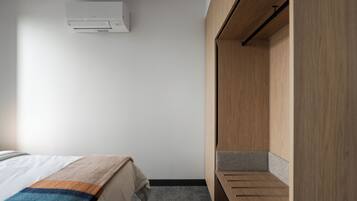 Una habitación de hotel con una cama, un armario de madera, una alfombra gris y un aire acondicionado blanco en la pared.