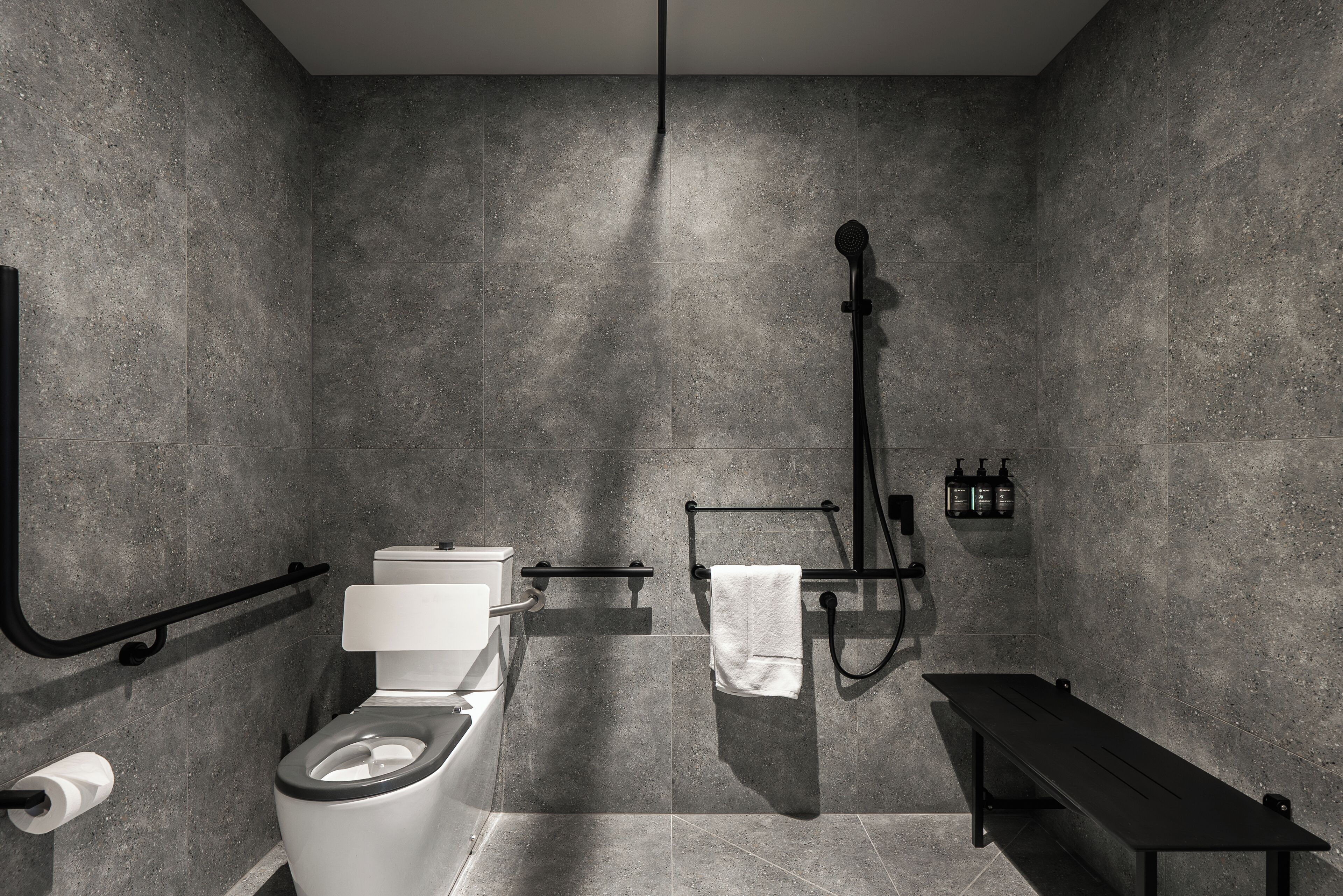 A modern bathroom with a toilet, bidet, towel rack, and bench.