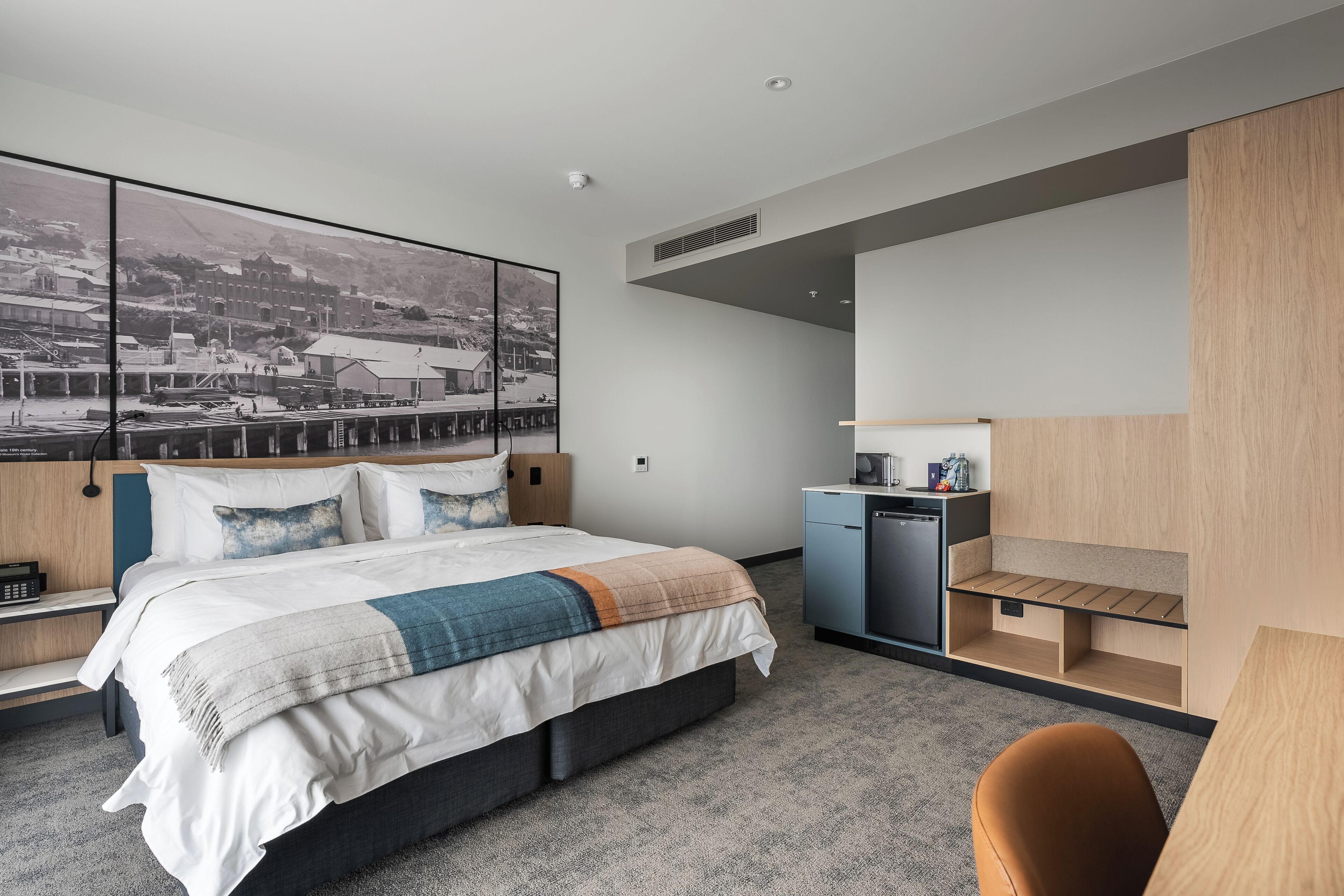 A modern hotel room with a large bed, a desk, and a built-in shelving unit.