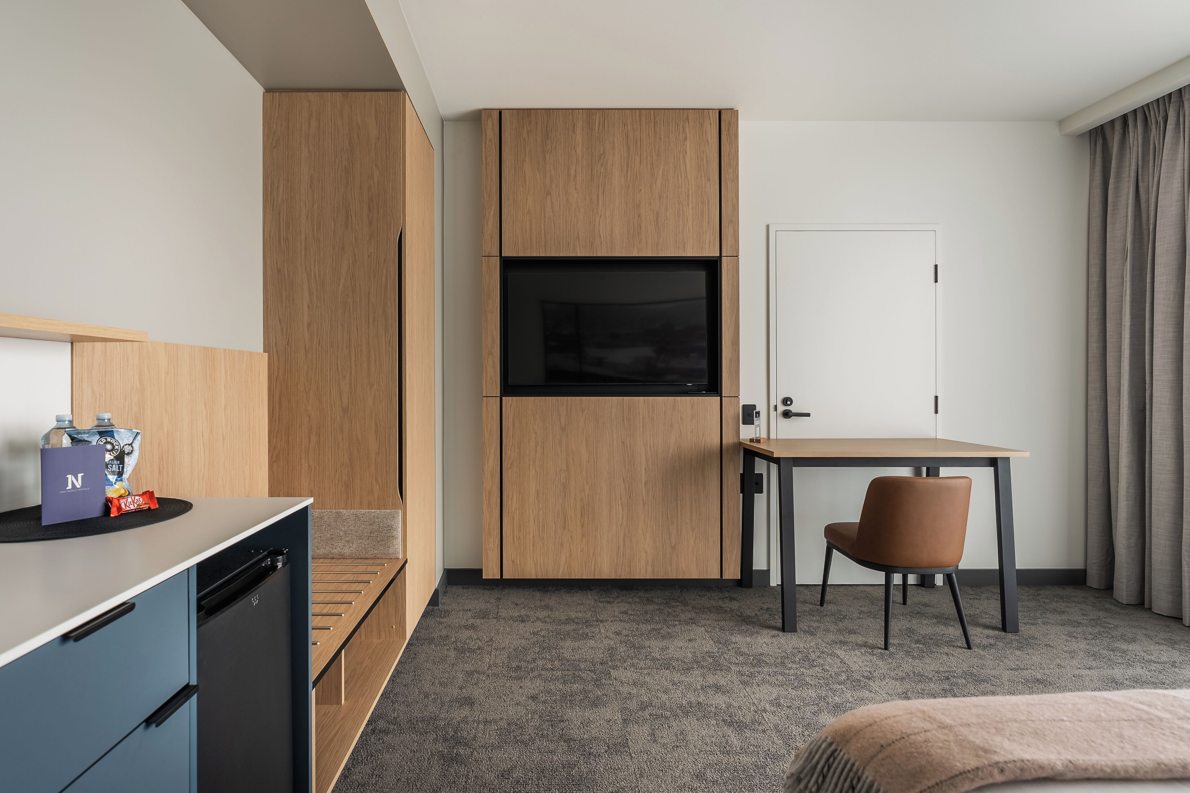 Una habitación de hotel con kitchenette, televisor, escritorio, silla y cama.