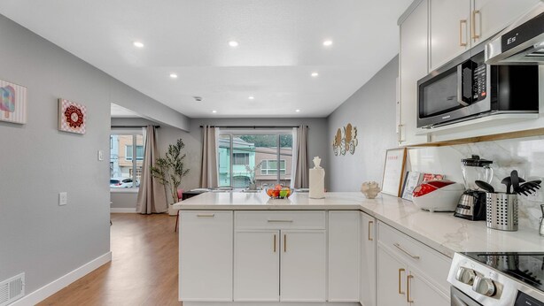A modern kitchen with white cabinetry, a central island, and stainless steel appliances including a microwave and oven.