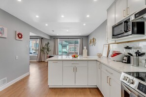 Une cuisine moderne avec des meubles blancs, un îlot central et des appareils en acier inoxydable, notamment un four à micro-ondes et un four traditionnel.