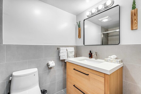 Une salle de bain moderne avec des toilettes blanches, un meuble-lavabo en bois et un miroir avec éclairage intégré.