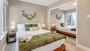 A bedroom with a large bed, bedside lamps, a mirror, and a macrame wall hanging.