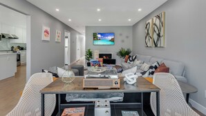 A modern living room with a dining table, sofa, and a TV mounted on the wall.