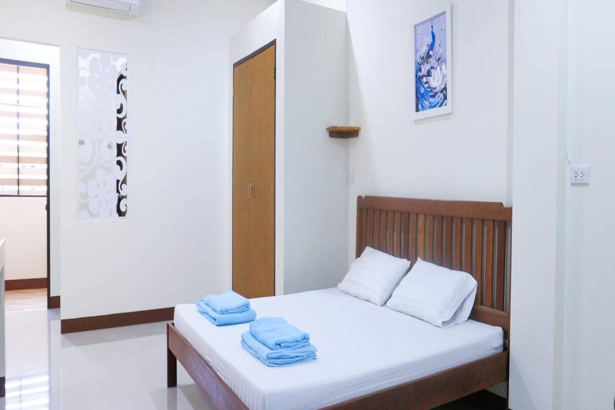 Un lit bien fait, avec des serviettes bleues, une tête de lit en bois et un climatiseur fixé au mur.