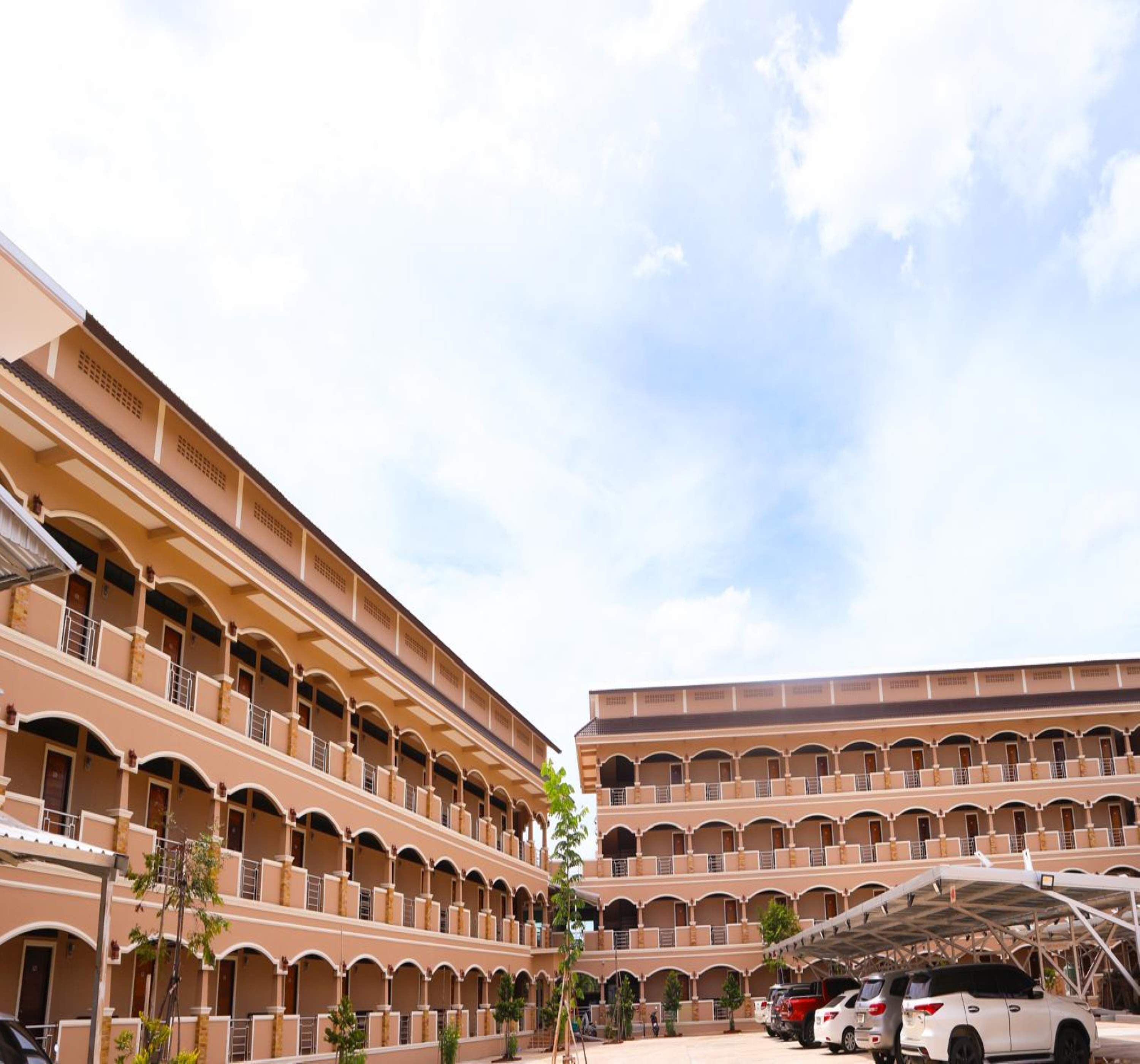 A multi-story hotel with a central courtyard, featuring balconies and a covered parking area.
