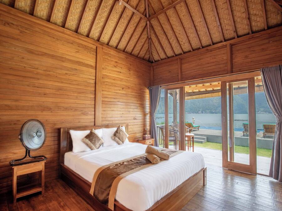 Un dormitorio de cabaña de madera con una cama, una mesita de noche, un ventilador y vistas al exterior.