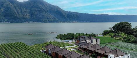 A lakeside resort with multiple wooden cabins, a swimming pool, and a view of a mountain range.