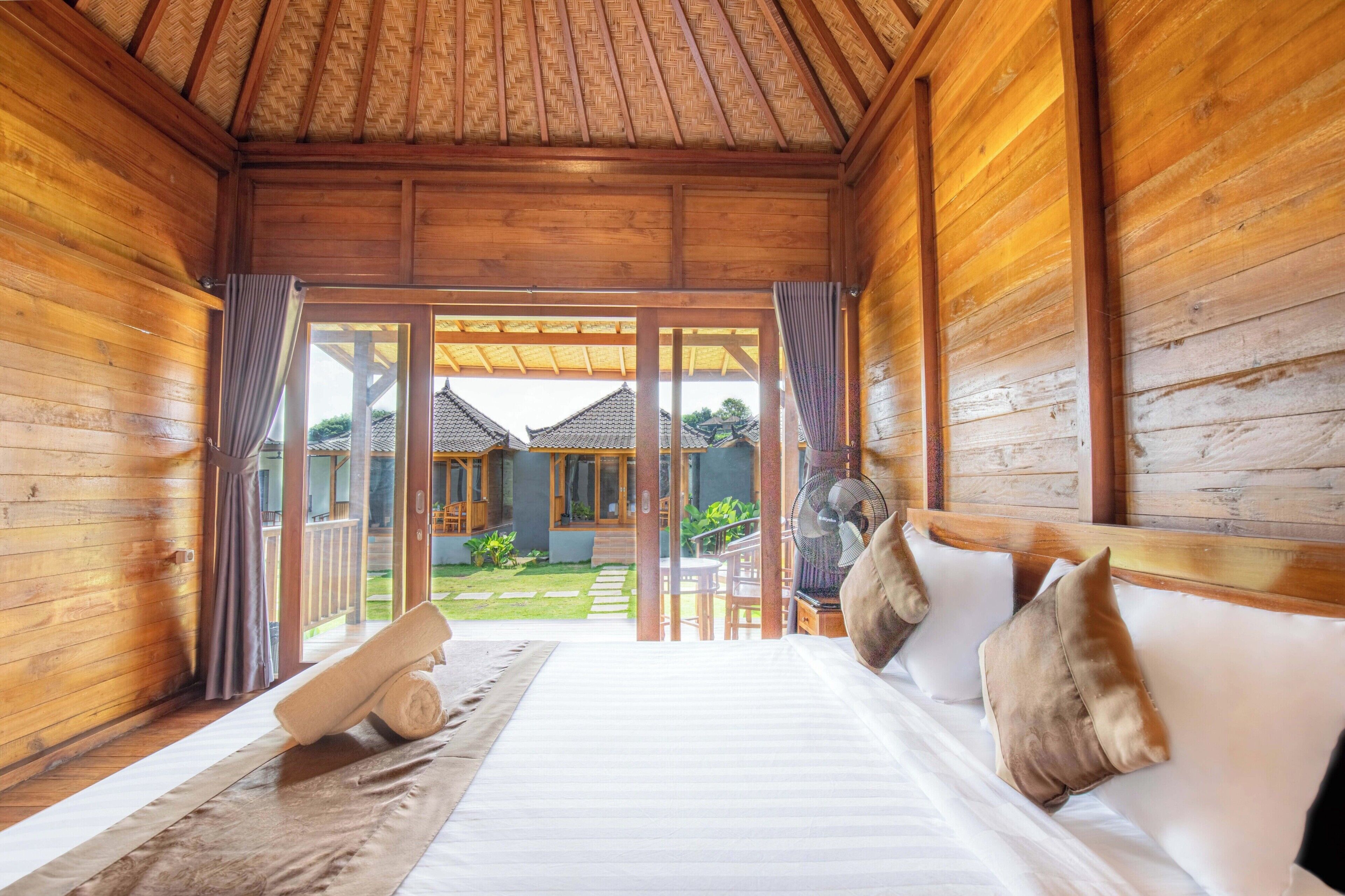 Una habitación de madera con una cama, almohadas y un ventilador.