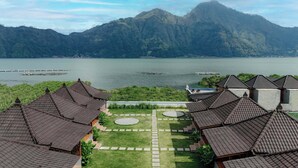 A resort with traditional tiled roofs, a central courtyard with stone pathways, and a view of a lake with mountains in the background. - D Sila’s Tepi Danu Villas Kintamani & Natural hot spring (Kintamani)