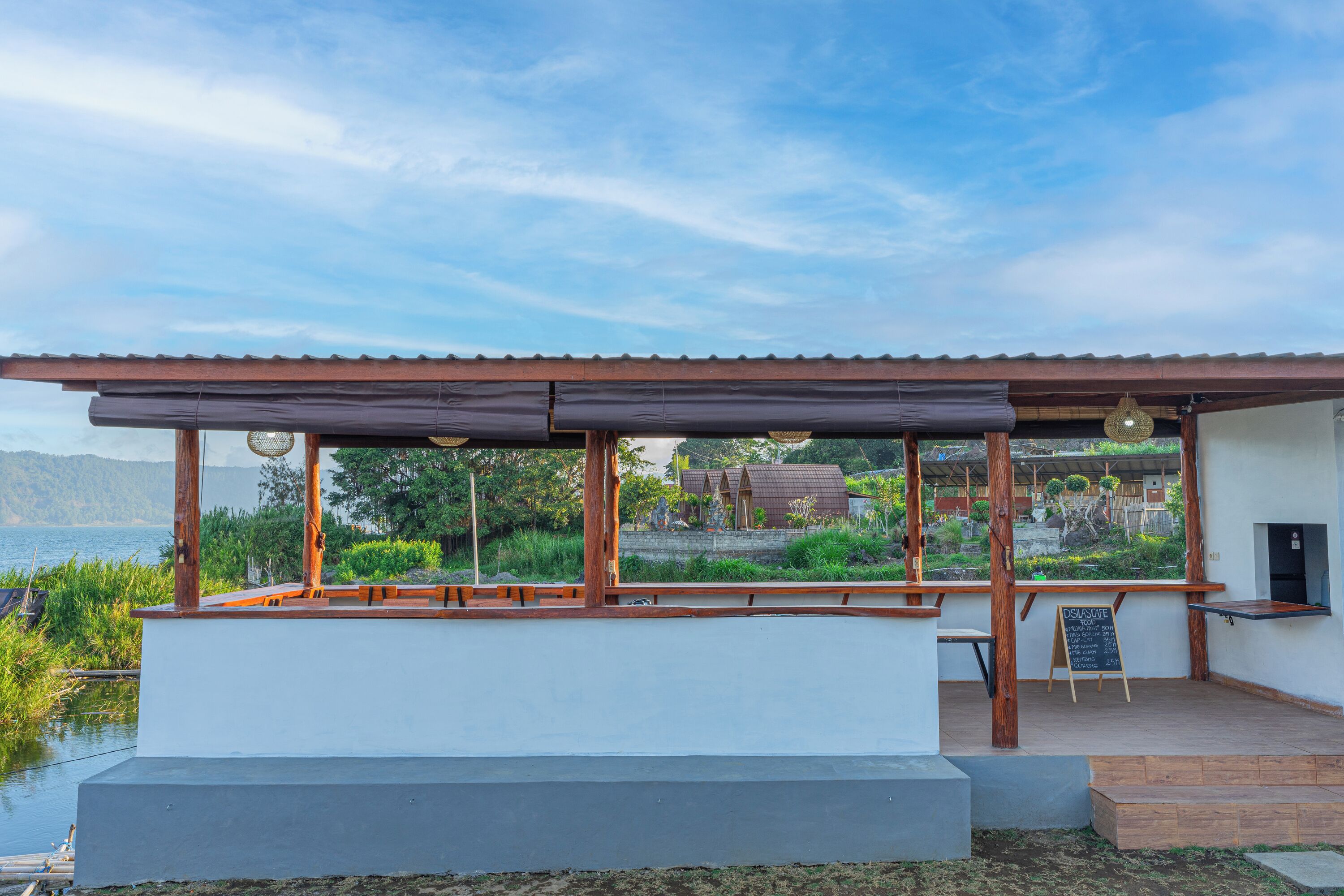 Un restaurante frente al agua con terraza techada, un menú en pizarra y vistas al lago y las colinas.