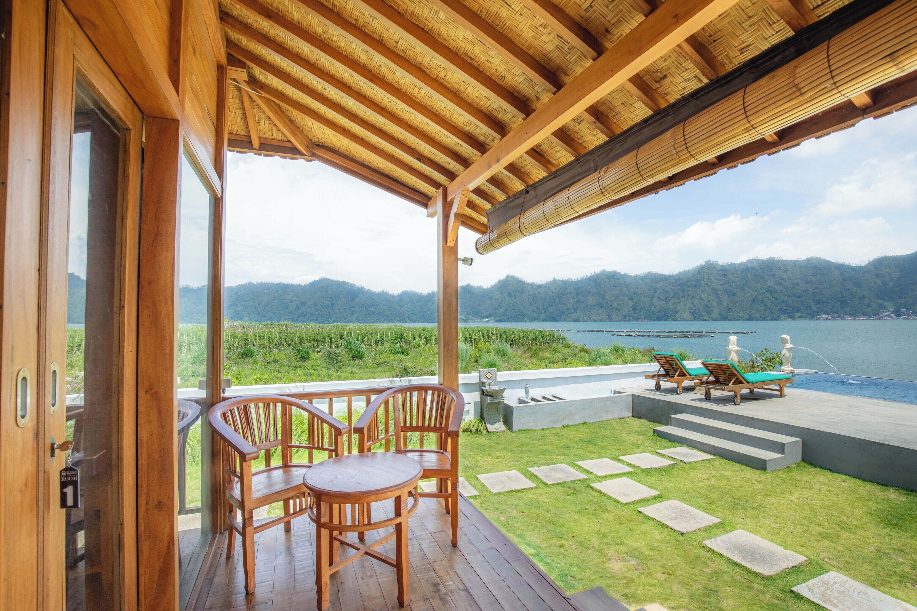 A wooden deck with a table and chairs, overlooking a lake and mountains.