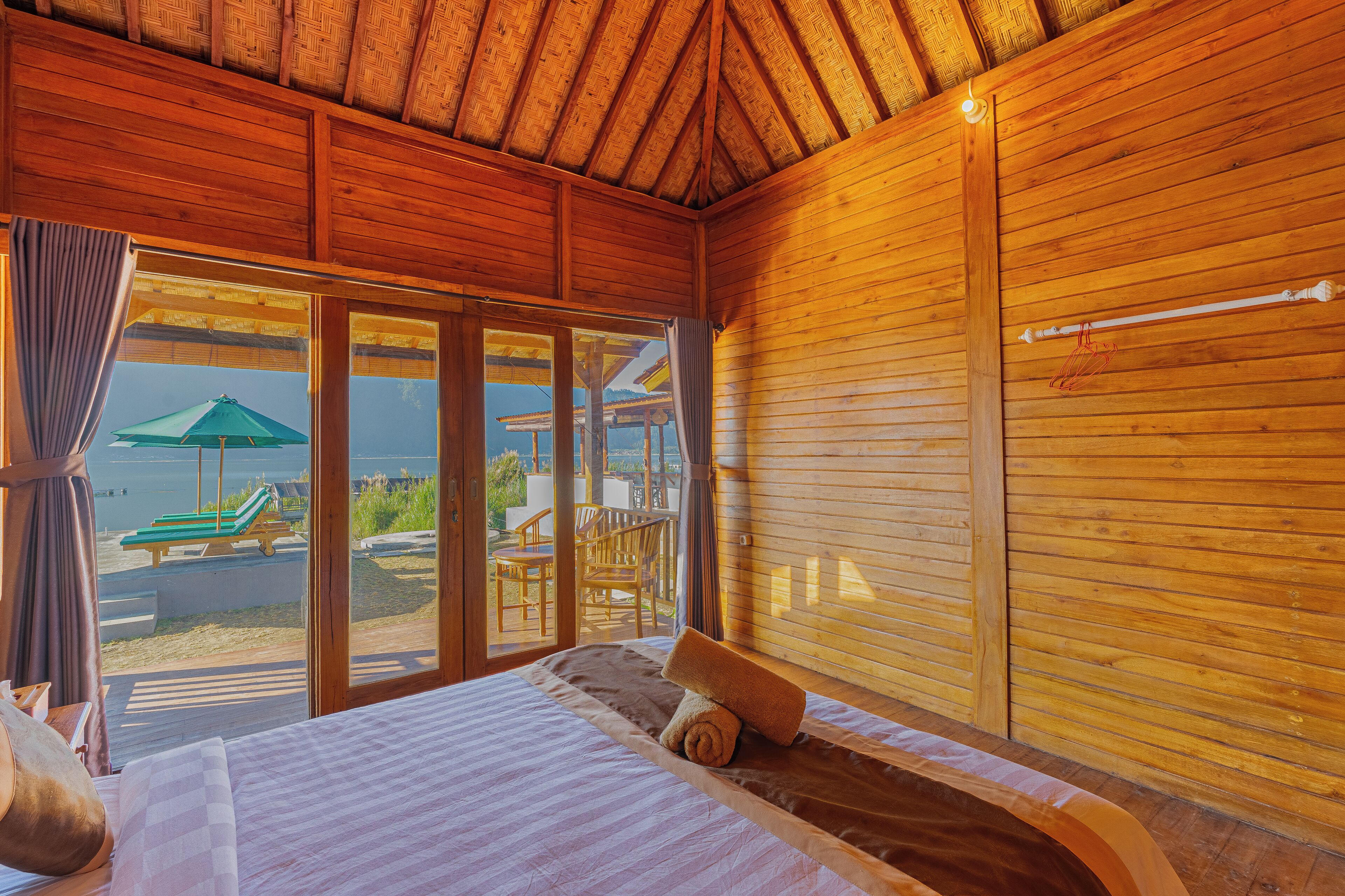 A wooden cabin room with a bed, a window, and a view of the beach.